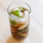 A mojito made with coke sitting on a wooden cutting board.