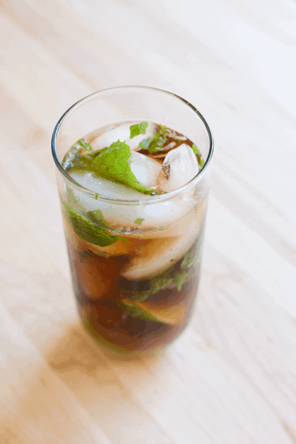 A cocktail with Coke, fresh mint and lime in a tall glass on a cutting board. 