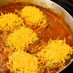 Green Chile and cheese topped pork chops in tomato sauce in a frying pan.