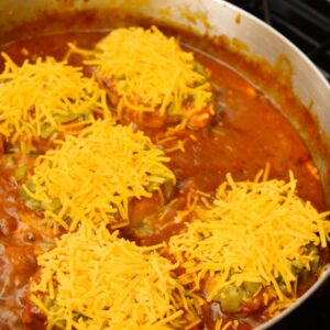 Green Chile and cheese topped pork chops in tomato sauce in a frying pan.