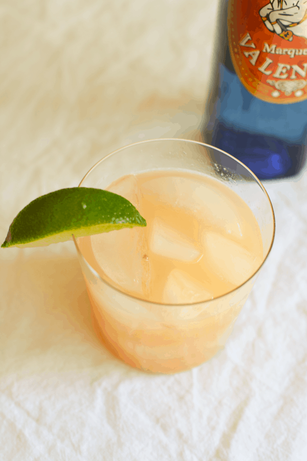 A cocktail glass with grapefruit cocktail next to a bottle of tequila. 