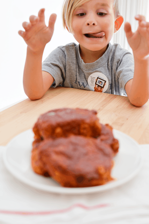 Little boy smiling with a plate of pork chops in front of them.