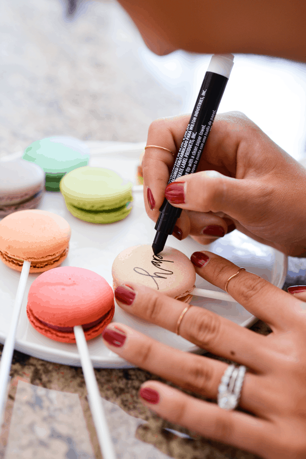 Woman writing on colorful macarons with edible ink pen.