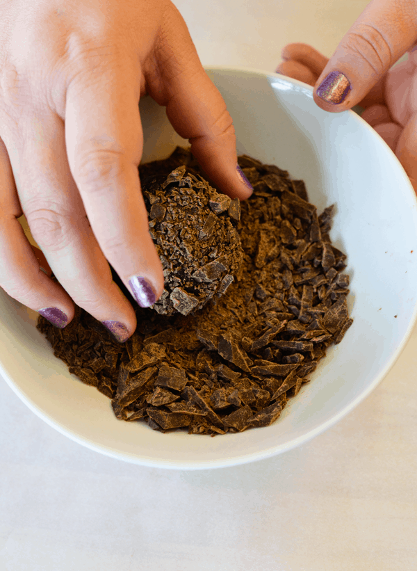 Woman rolling a cookie ball in a bowl of chopped chocolate to coat.