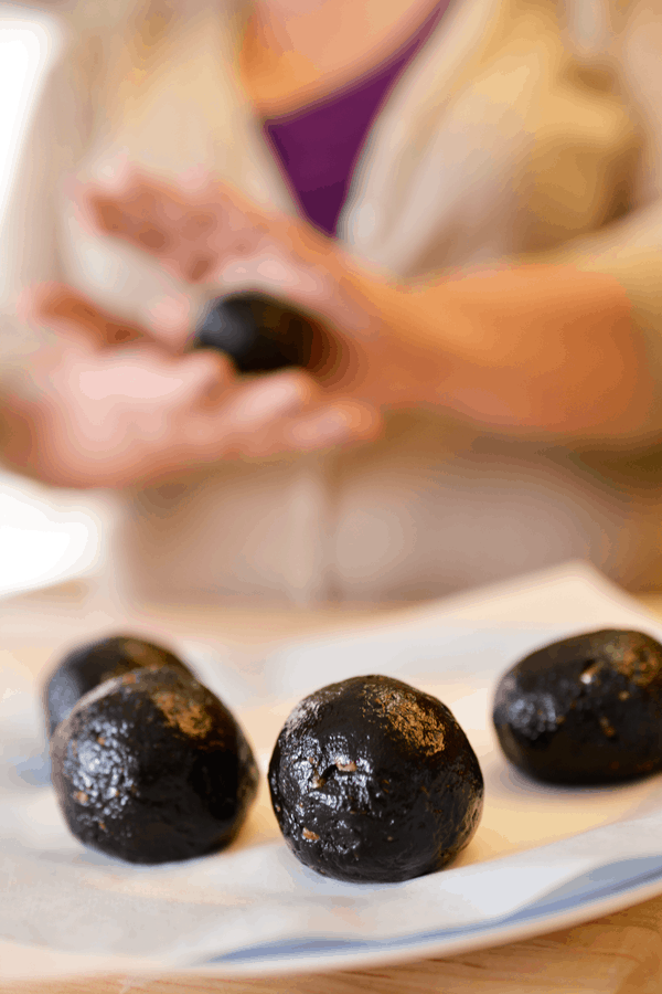 Close up of cookie balls with a woman rolling one between her hands in the background. 