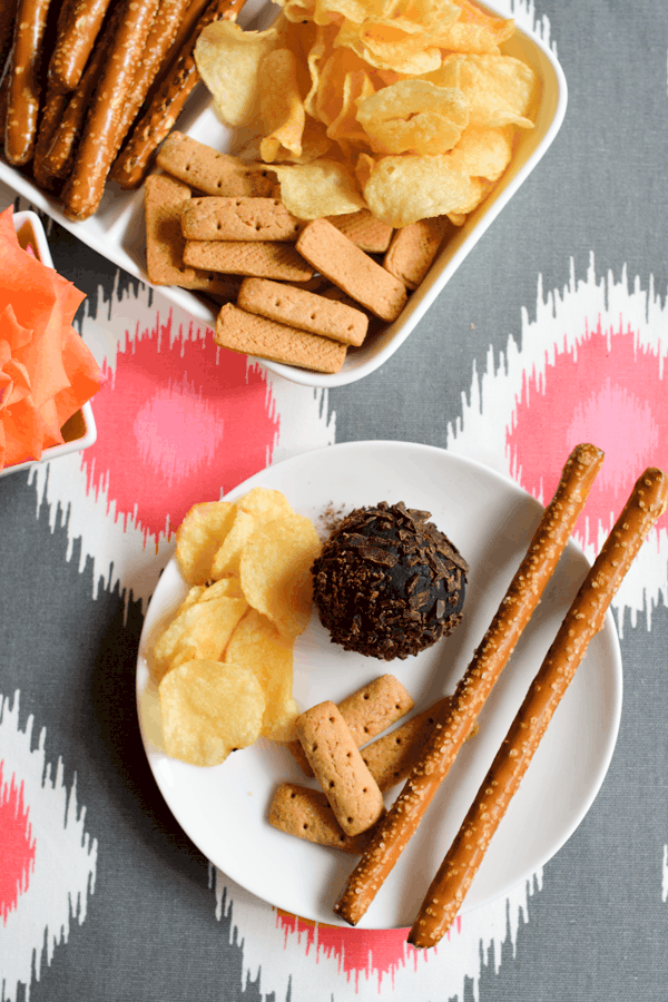 A small plate with a dessert cookie ball next to chips, pretzel rods and graham sticks. 