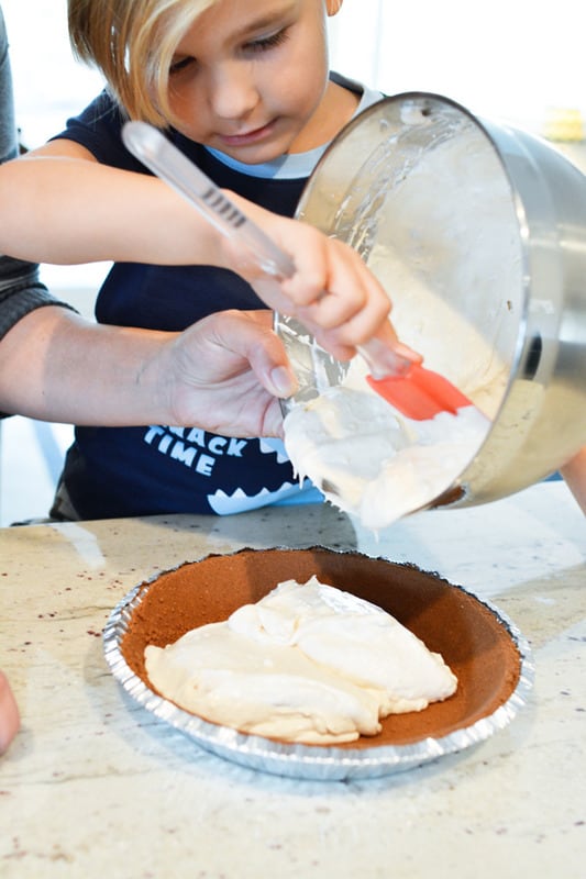Mother and child scraping creamy filling into a pie case.