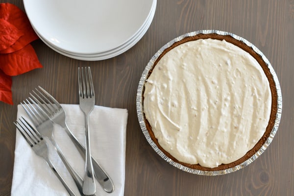 A peanut butter pie on the table next to forks and a stack of plates.