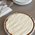 Peanut butter pie on the counter with a stack of plates and forks.