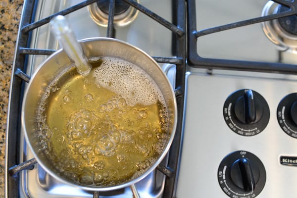 Overhead photo of sugar boiling in a saucepan on the stove with a candy thermometer.