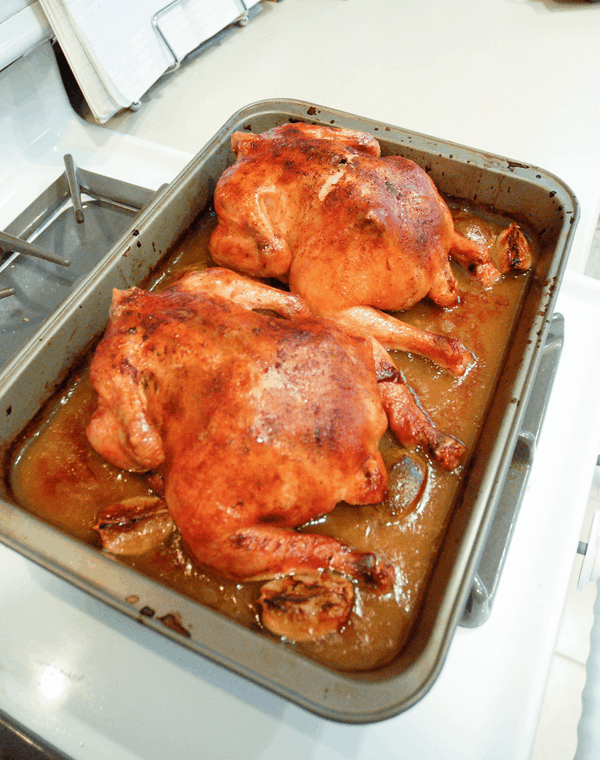 A roasting pan with two whole chickens that have been roasted.