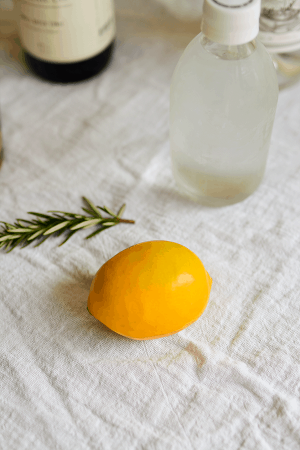 A meyer lemon on a table next to a sprig of rosemary and a bottle of club soda. 