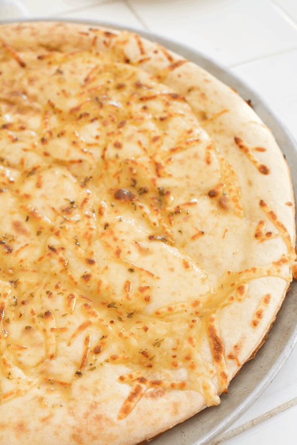 Close up of a buttered pizza crust on a pizza pan. 