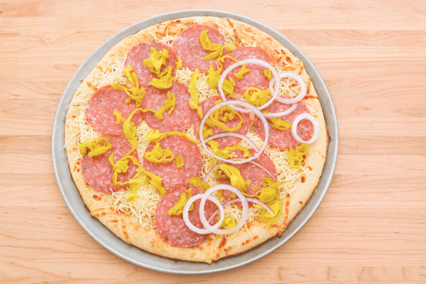 Overhead shot of a salami pizza with pepperoncini, red onion and cheese before it's baked. 