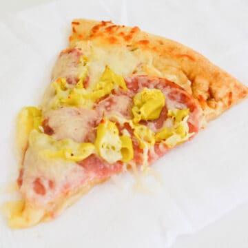 A slice of pepperoncini and salami pizza on a white napkin.