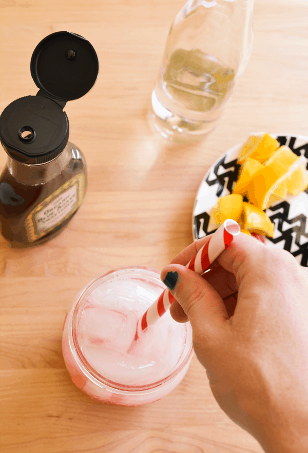 Stirring muddled raspberry lemonade with a straw.