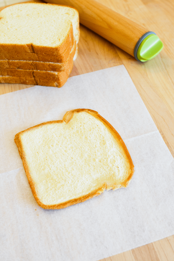 A pice of King's Hawaiian Bread on a piece of white waxed paper on a wooden cutting board next to a stack of more bread and a rolling pin.