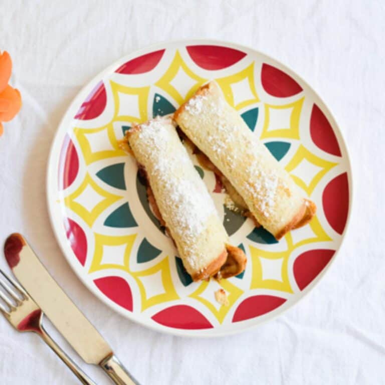 Close up of a plate with 2 pieces of Hawaiian bread rolled up and dusted with powdered sugar.