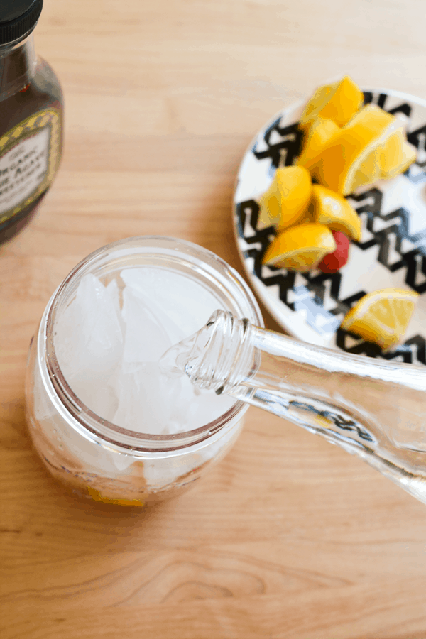 Water being poured over ice in a jar of muddled fruit.