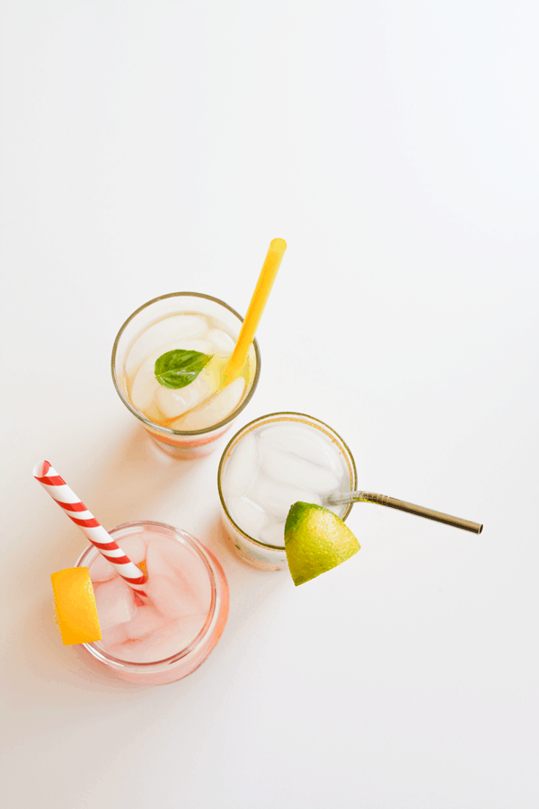 Delicious fruit infused water in glasses pictured top down on a white background.