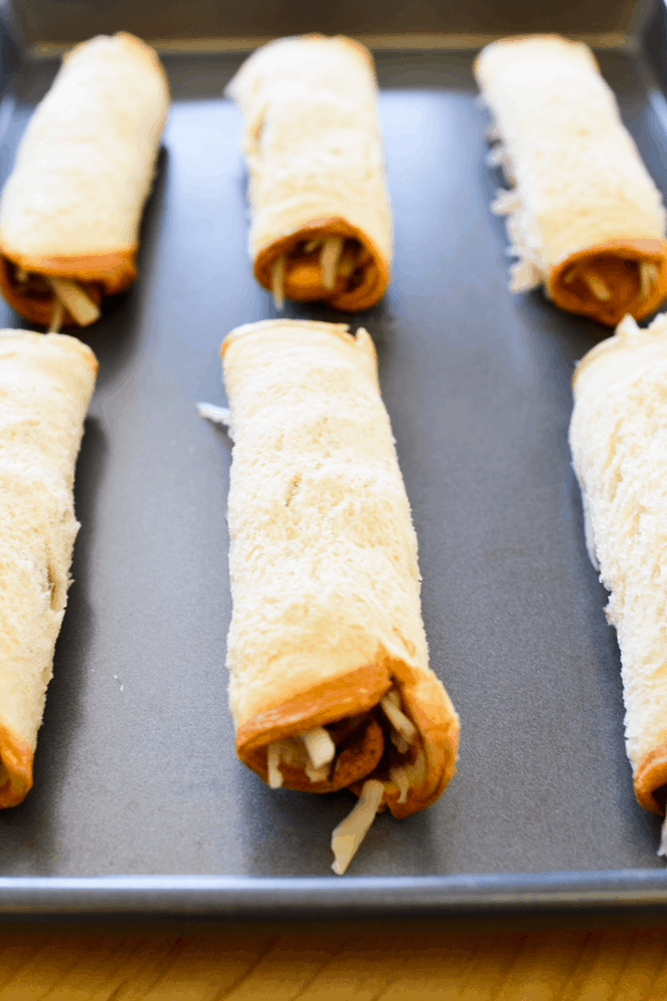 Hawaiian bread rolled up with cheese and ham on a cookie sheet. 