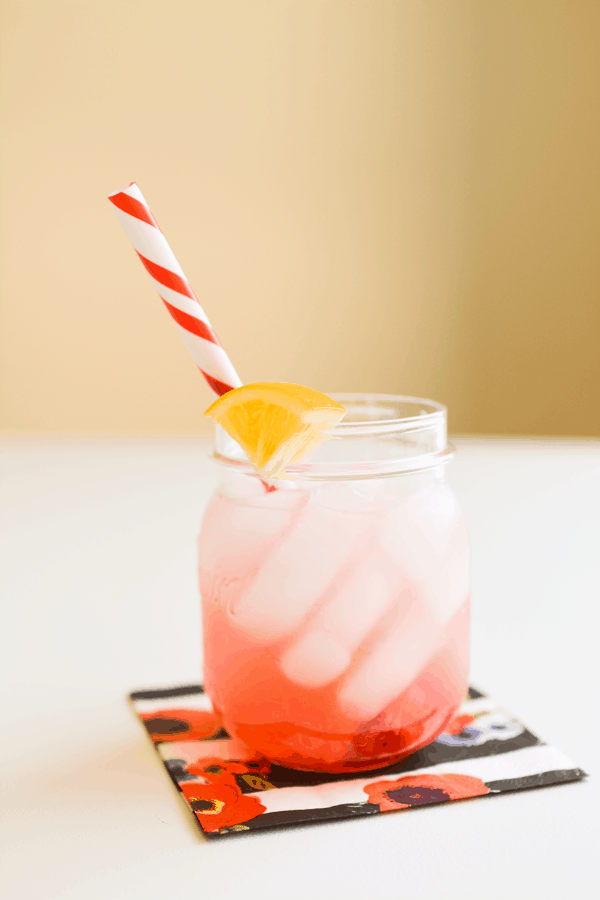 Muddled raspberry lemonade in a mason jar garnished with a lemon swedge and a red and white striped paper straw.