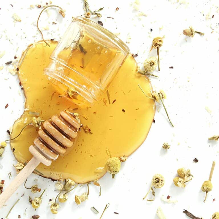 A jar on its side with honey spilled on a white table.