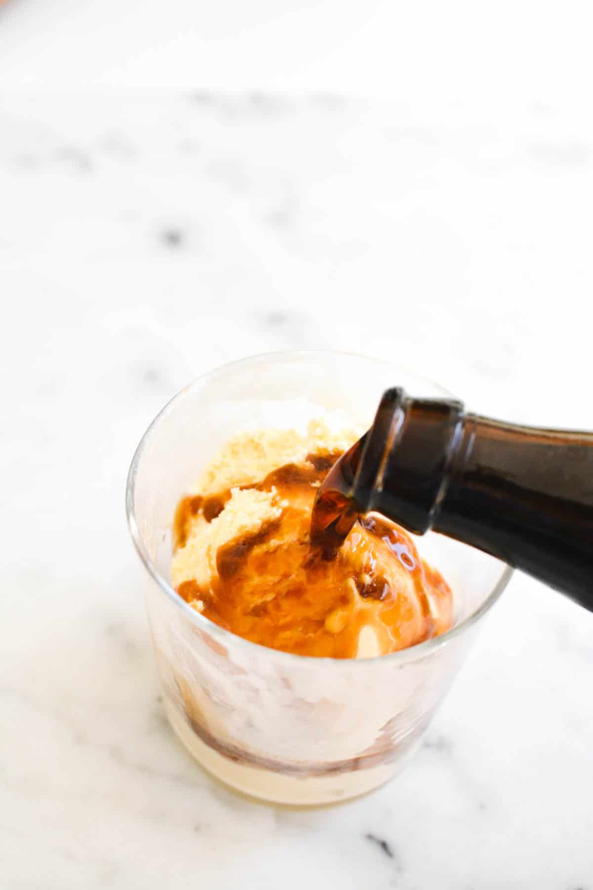 Beer being poured over ice cream in a short glass for an alcoholic float.