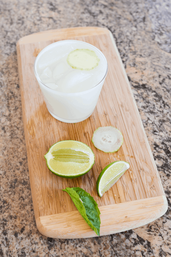 Cucumber Basil Vodka Skinny Cocktail Idea next to sliced cucumbers, fresh basil and lime wedges.
