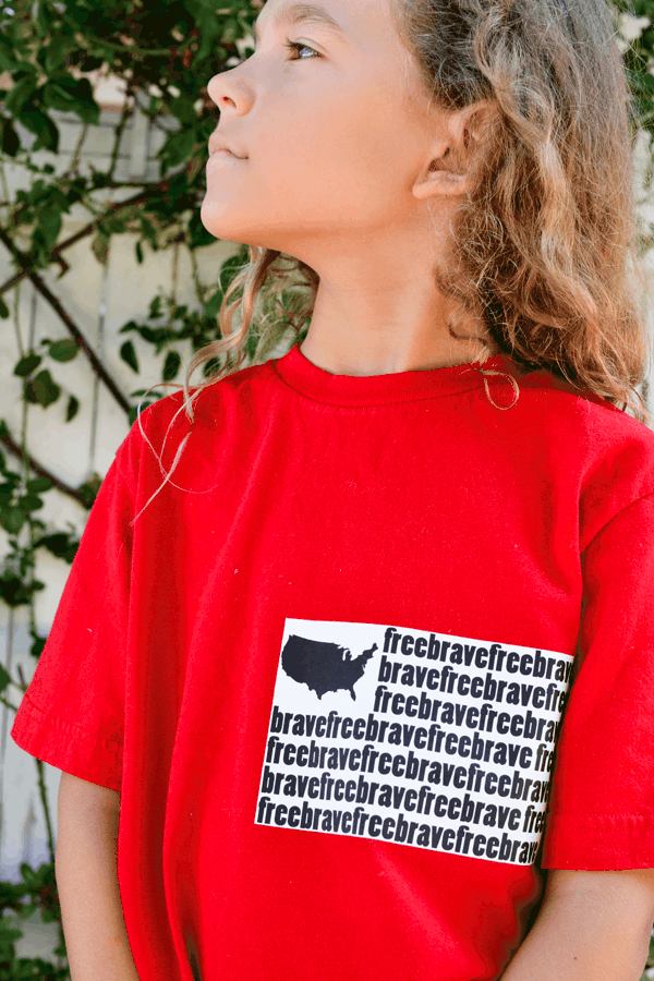 kid wearing a red t shirt with the words free and brave on it with a small iron on of the United States outline.