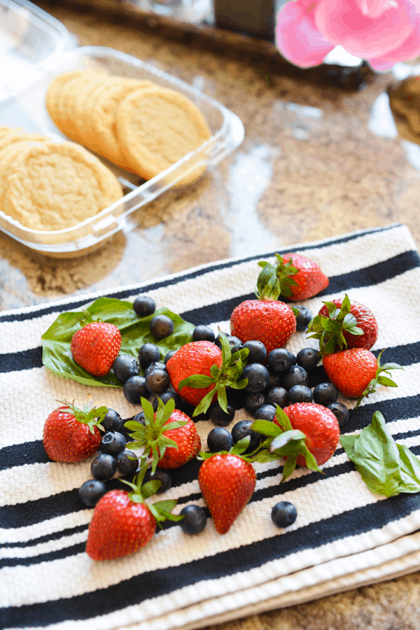 Fresh strawberries, basil and blueberries on a towel next to a container of store-bought sugar cookies.