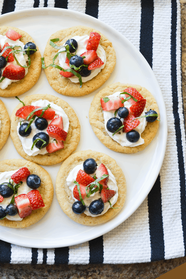 Fruit desserts are a great idea when you need to bring a dish to a potluck! Berry Basil Dessert Bruschetta with Sugar Cookies fruit dessert on a white serving platter.