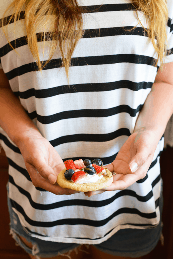 Girl holding a sugar cookie topped with whipped cream and a mix of fresh berries and basil. 