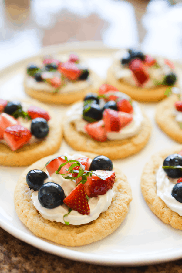White plate of fruit bruschetta and whipped cream topped sugar cookies.
