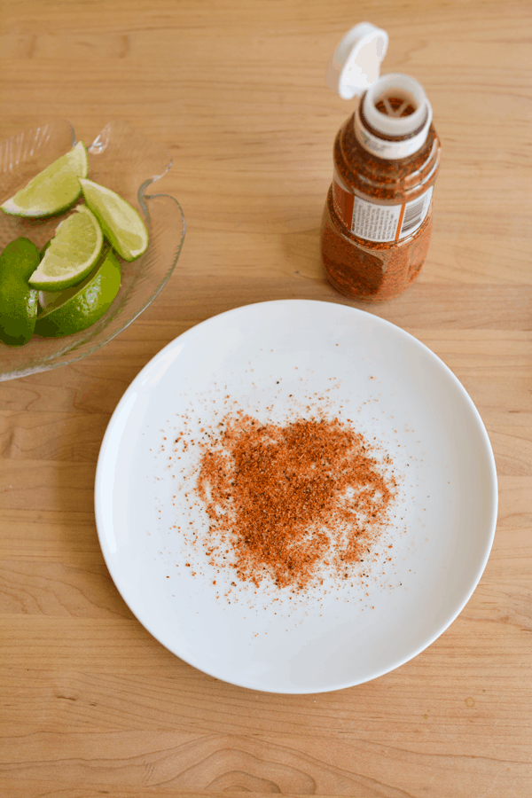 Tajin on a plate with the bottle of Tajin next to it and a plate of sliced limes. 