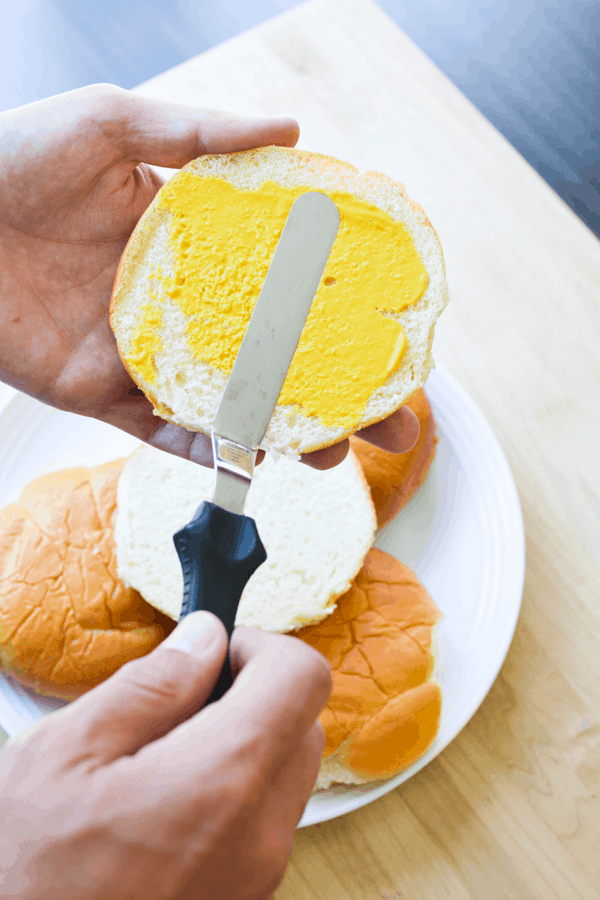 Spreading mustard on a hamburger bun before grilling. 