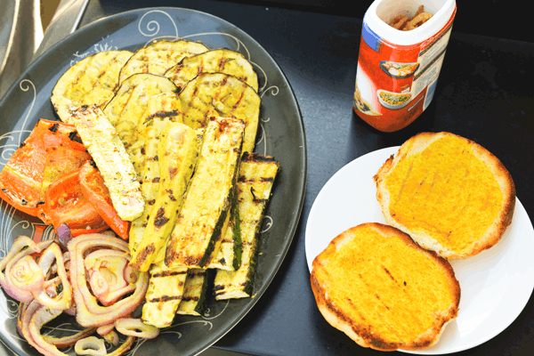 A plate of grilled vegetables next to a mustard grilled bun and can of friend onion strings.
