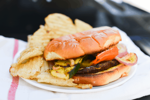 A finished grilled vegetable sandwich on a plate with potato chips. 