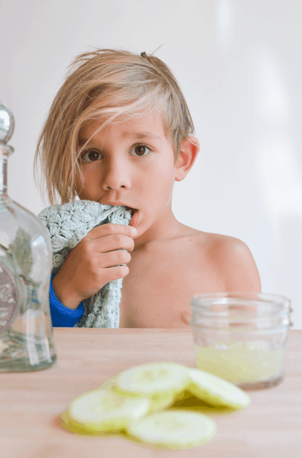 Boy standing behind the table with his blanket in his mouth.