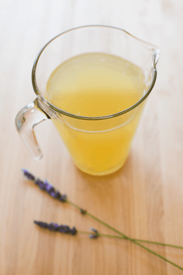 Pitcher of homemade lavender lemonade on a cutting board next to lavender sprigs