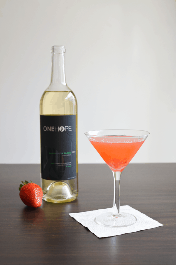 Strawberry and Sauvignon Blanc Martini on a cocktail napkin next to a bottle of wine and a fresh strawberry.