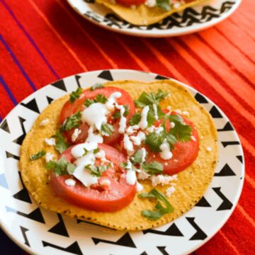 Close up of a tostada with sliced tomatoes and crema sauce.