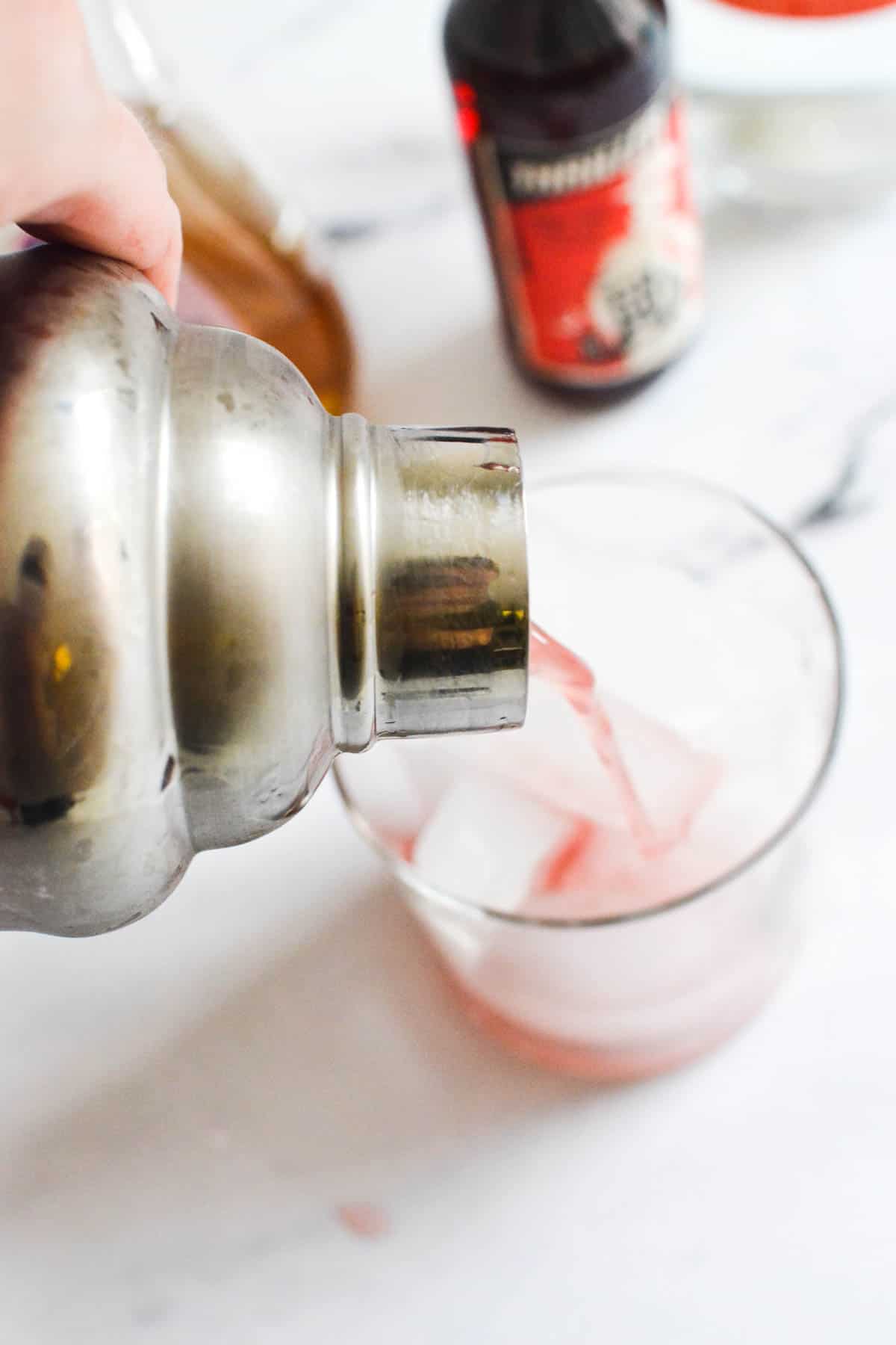 Close up of a cocktail pouring out of a shaker into a cocktail glass with ice.