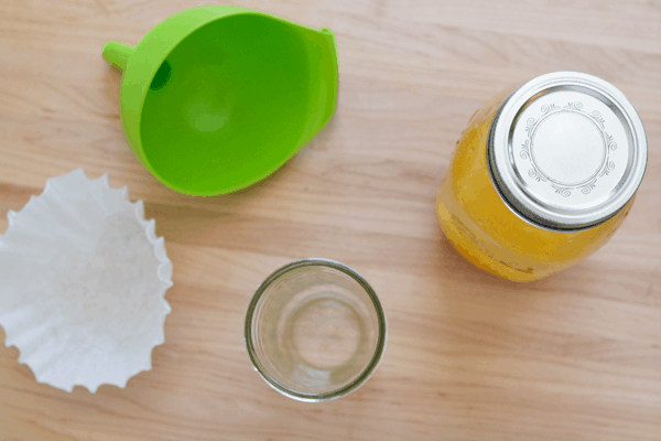 A jar of homemade orange infused vodka next to an empty jar, coffee filter and funnel. 