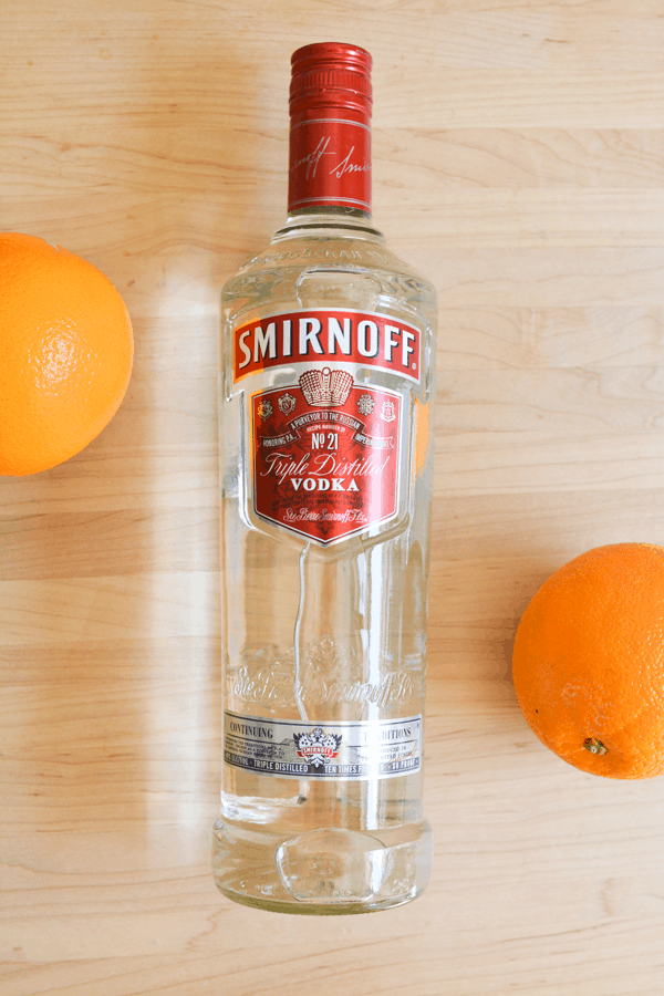 A bottle of Smirnoff vodka laying on a wooden counter with oranges next to it. 