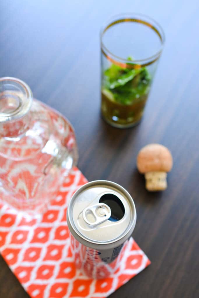 An open can of club soda on a table next to a Patron bottle and cocktail glass.