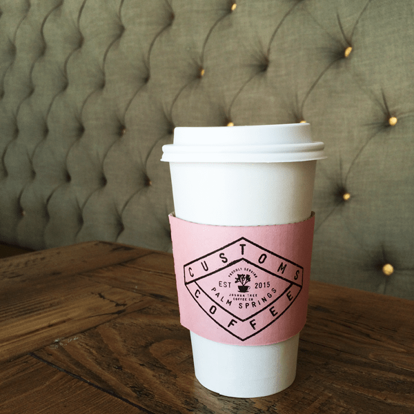 A cup of coffee on a wooden table with a design on the sleeve.