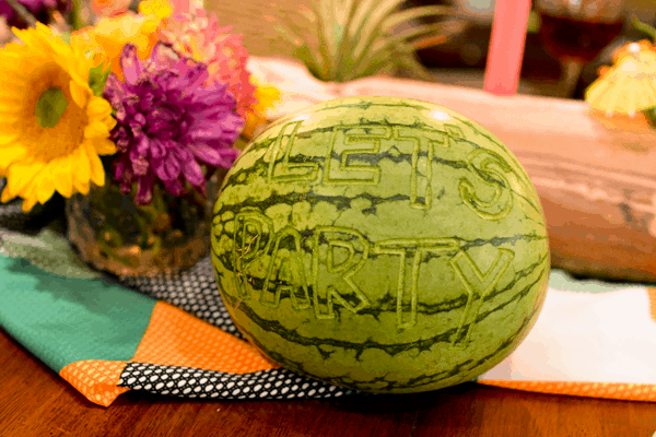 A carved watermelon with words on it on a party table. 