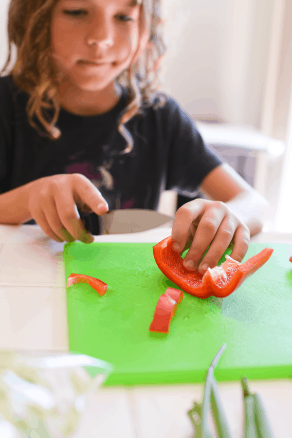 Kid cutting a red bell pepper with a knife on the counter. 