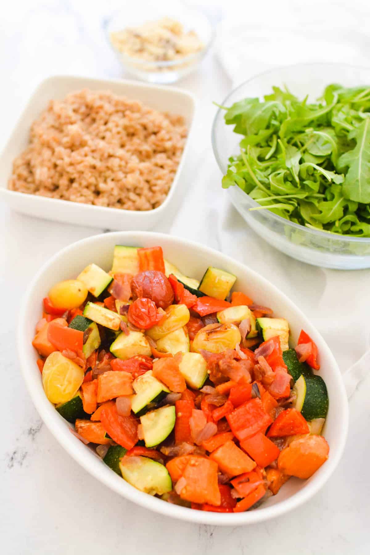 Bowls on a table of items to make into a farro bowl lunch.